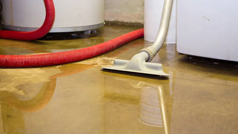 Wet vacuum with a red hose pulling water from a floor beside a water heater